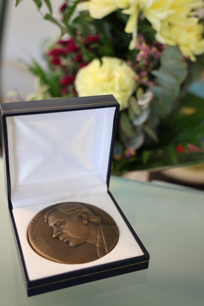 Pronssinen mitali ja taustalla kukkia